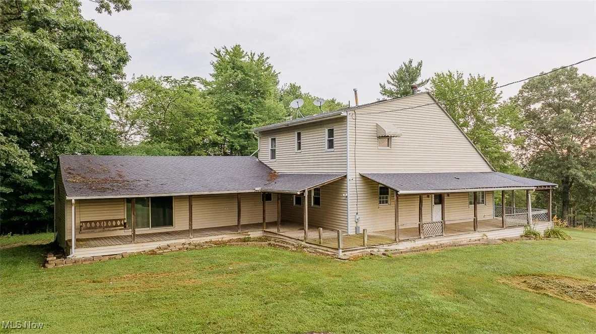 Side of house featuring a lawn, roof with shingles, a porch, and a patio