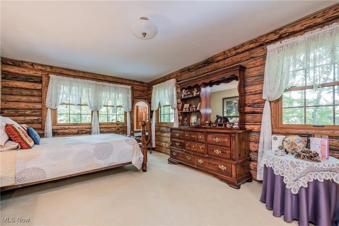 Bedroom with log walls, carpet, and wallpapered walls