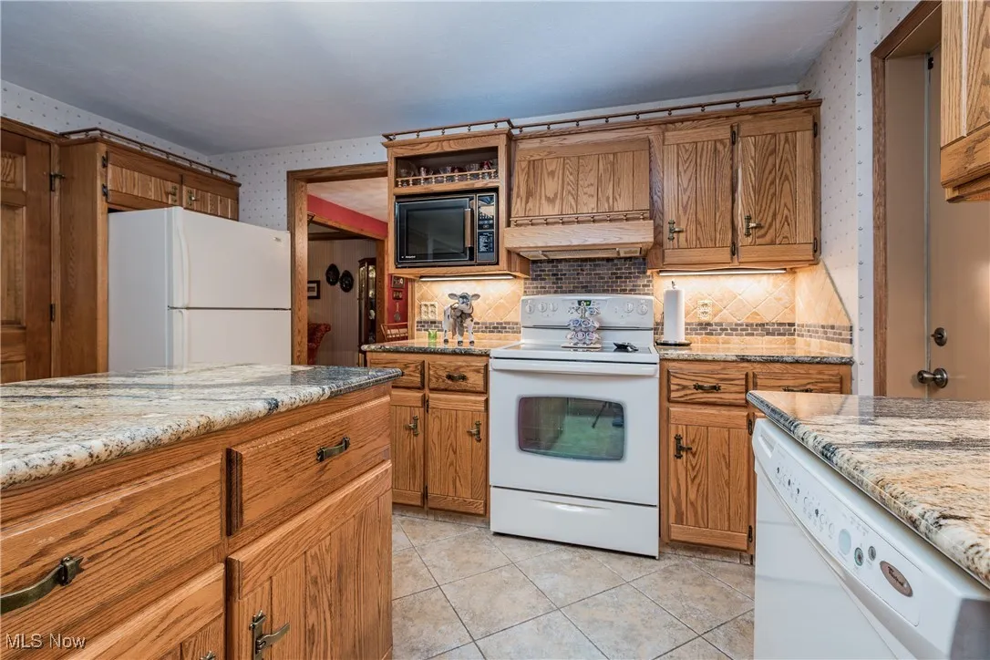 Kitchen with white appliances, wallpapered walls, under cabinet range hood, and brown cabinetry