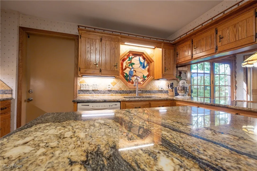 Kitchen featuring a sink, tasteful backsplash, brown cabinets, stone countertops, and dishwashing machine