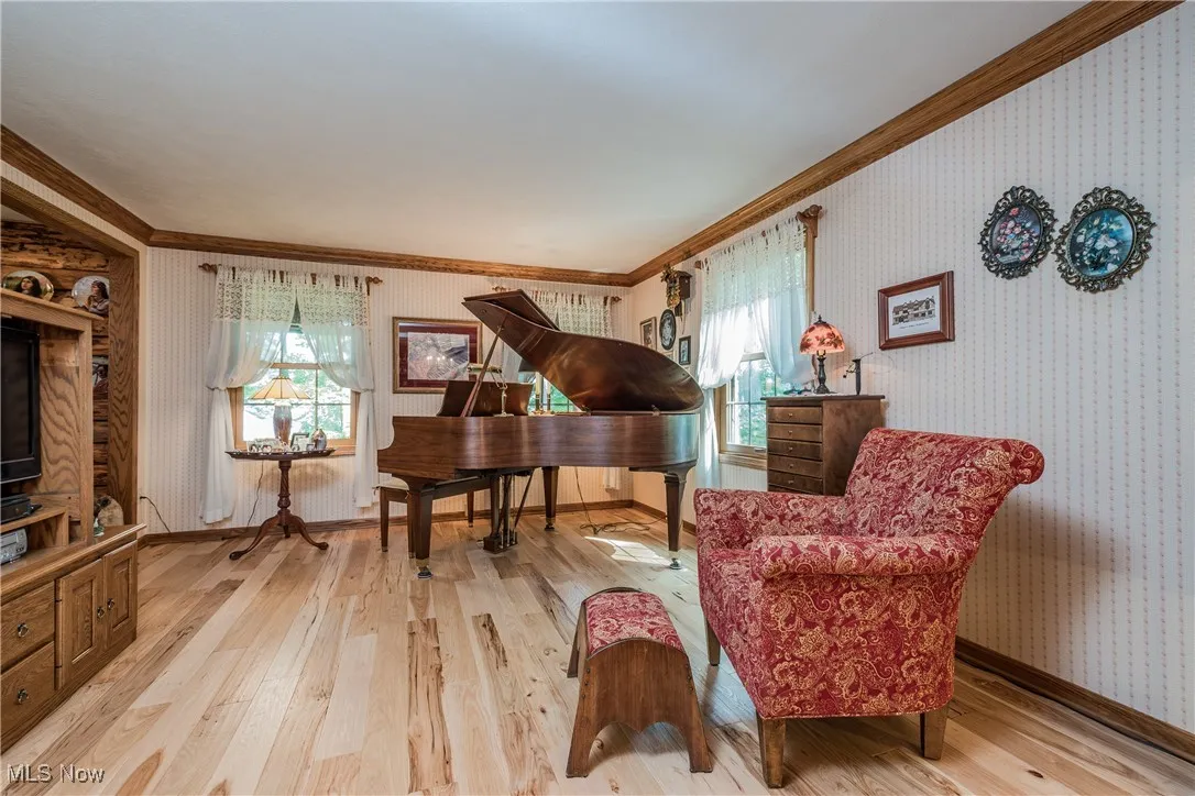 Sitting room featuring crown molding, wallpapered walls, light wood-style flooring, and baseboards