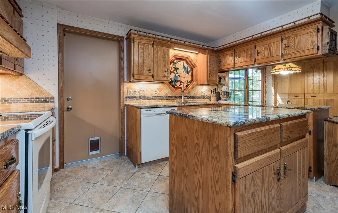 Kitchen with white appliances, a sink, backsplash, light stone counters, and brown cabinetry