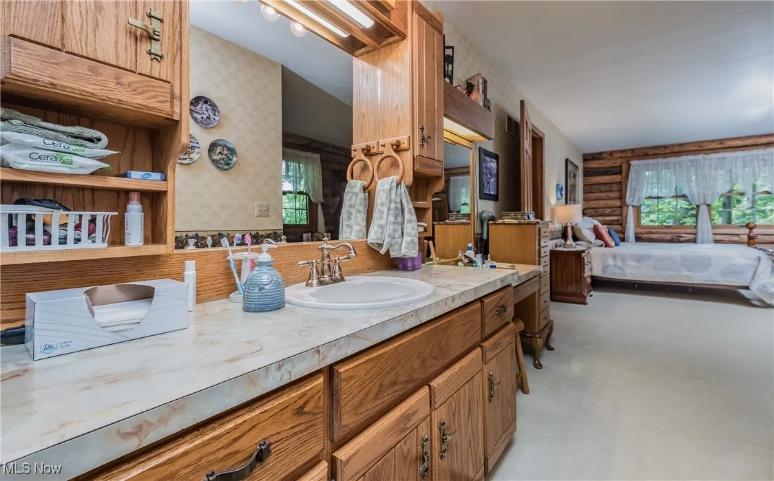 Ensuite bathroom with wallpapered walls, vanity, and log walls