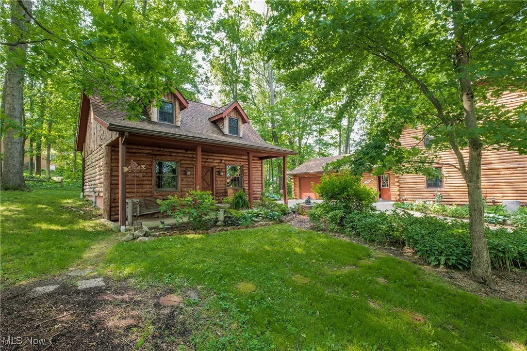 Log-style house with a front yard, log exterior, roof with shingles, and covered porch