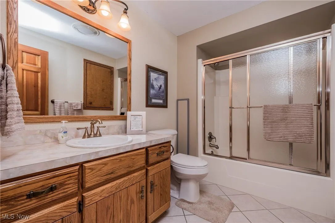 Full bath with vanity, tile patterned flooring, toilet, and bath / shower combo with glass door