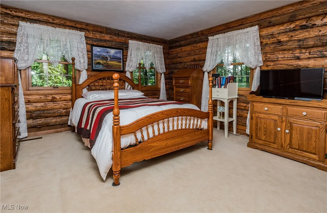 Bedroom featuring multiple windows, light colored carpet, and log walls