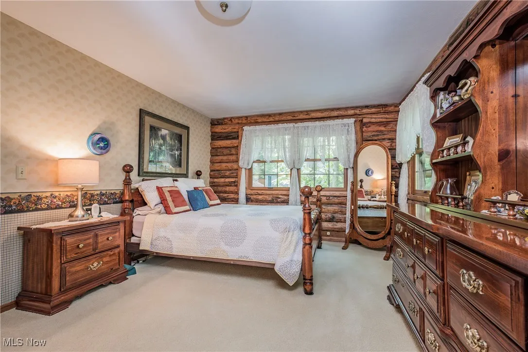 Bedroom with wallpapered walls, rustic walls, and light carpet