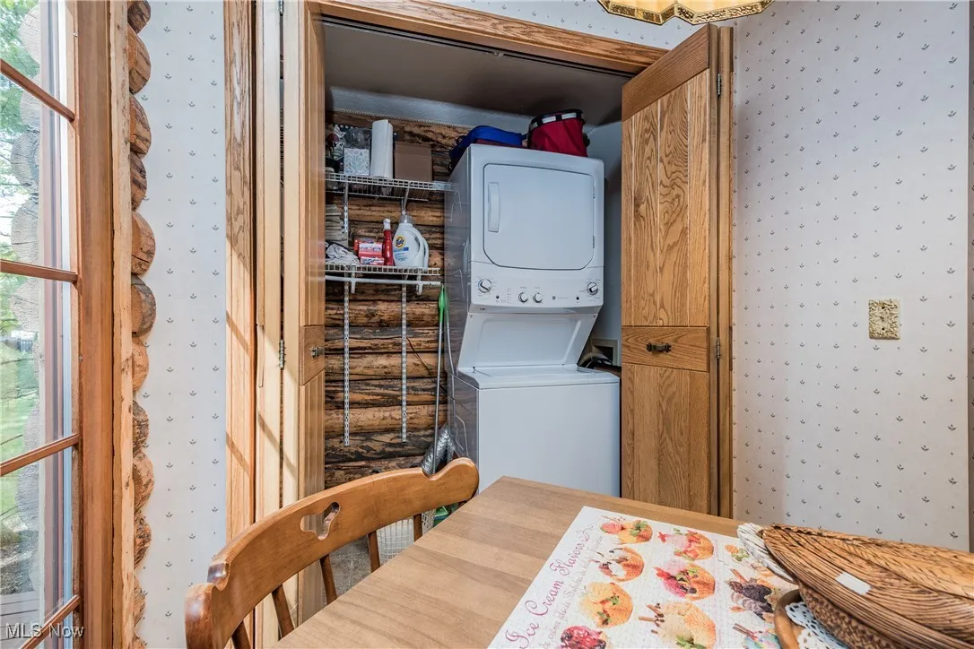 Laundry room with wallpapered walls, stacked washing machine and dryer, and plenty of natural light