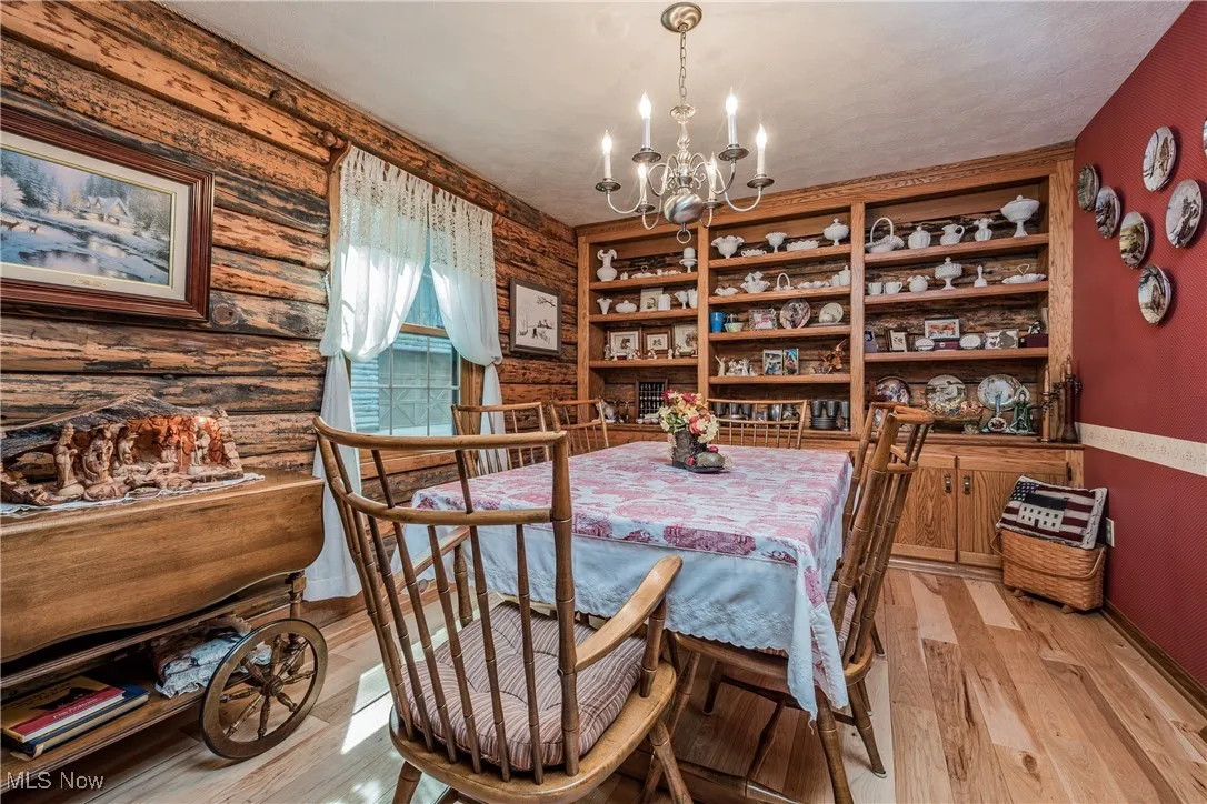 Dining area with a chandelier, light wood-type flooring, baseboards, and rustic walls