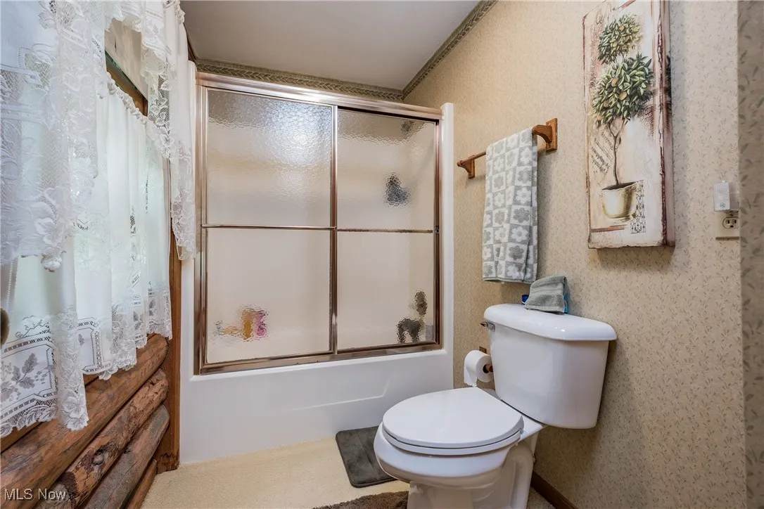 Bathroom featuring combined bath / shower with glass door and toilet