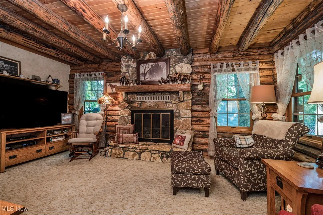 Carpeted living area with wooden ceiling with exposed beams, a chandelier, healthy amount of natural light, a fireplace, and log walls