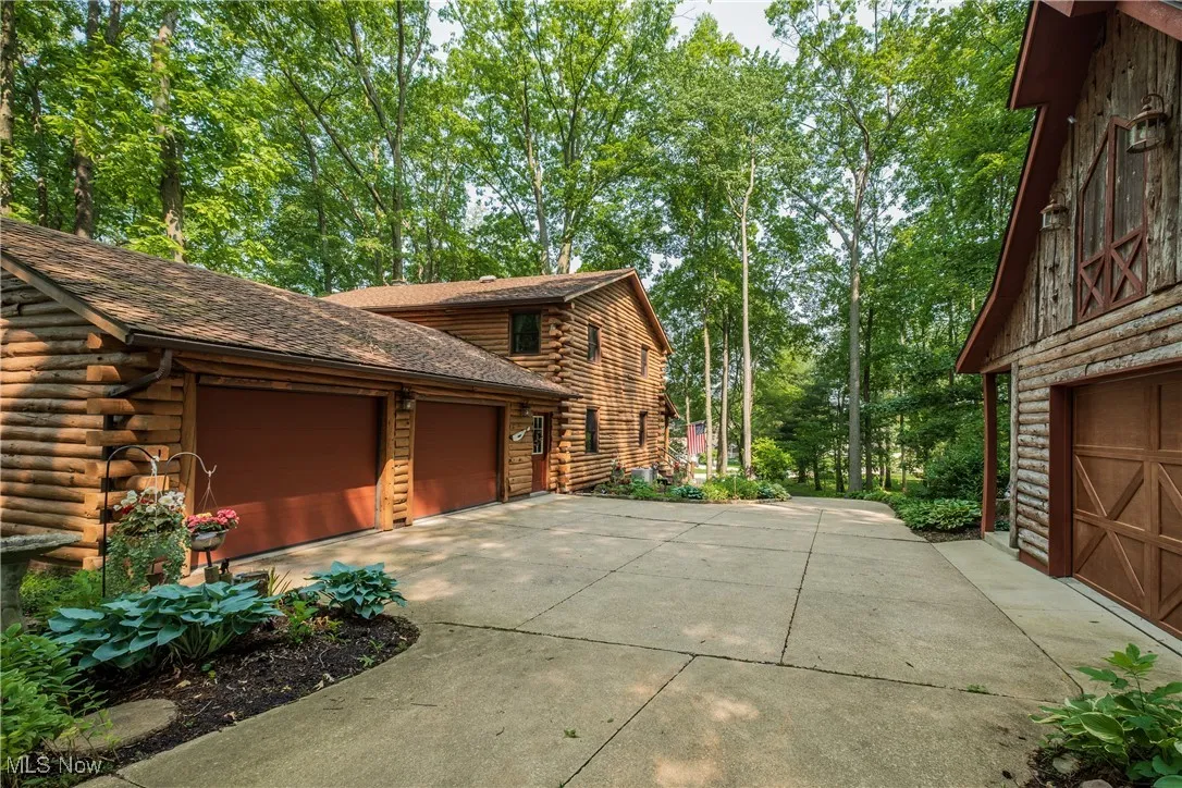 View of side of home with log exterior, concrete driveway, an attached garage, and an outbuilding
