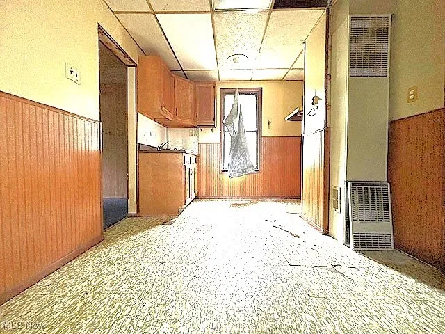Corridor with a wainscoted wall, wood walls, a heating unit, and a drop ceiling