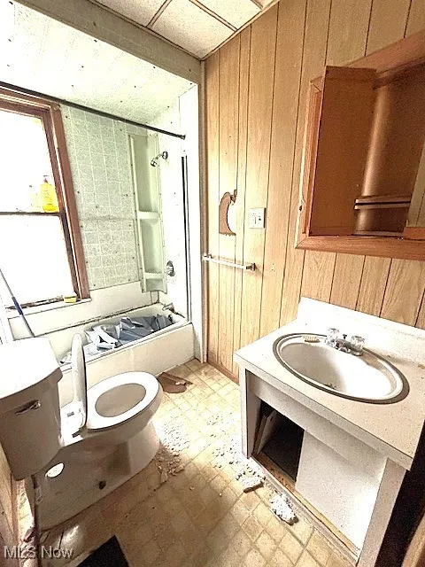 Full bathroom featuring tile patterned floors, wood walls, bathing tub / shower combination, and vanity