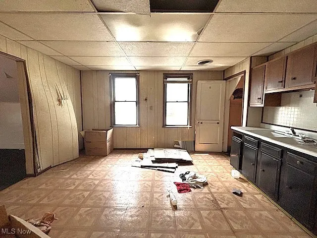 Kitchen featuring light floors, a drop ceiling, light countertops, wood walls, and tasteful backsplash