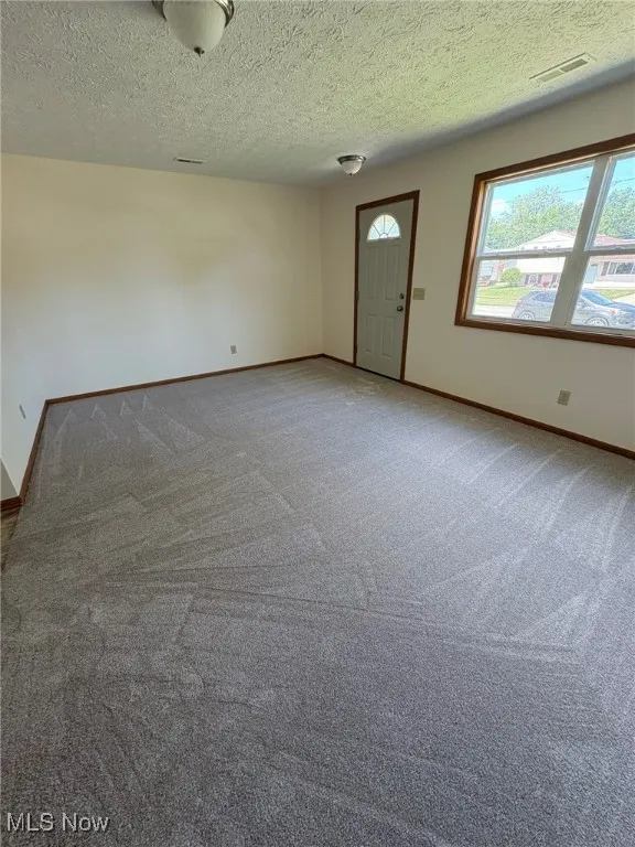Carpeted empty room with a textured ceiling and baseboards