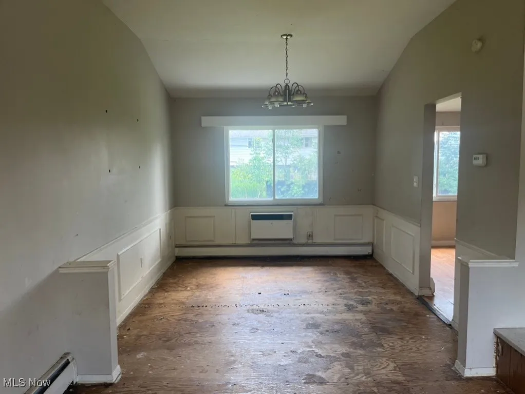 Unfurnished dining area featuring a chandelier, lofted ceiling, a wainscoted wall, a decorative wall, and a baseboard heating unit