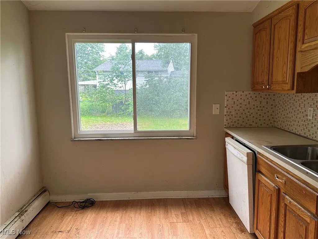 Kitchen featuring baseboard heating, backsplash, brown cabinets, and white dishwasher