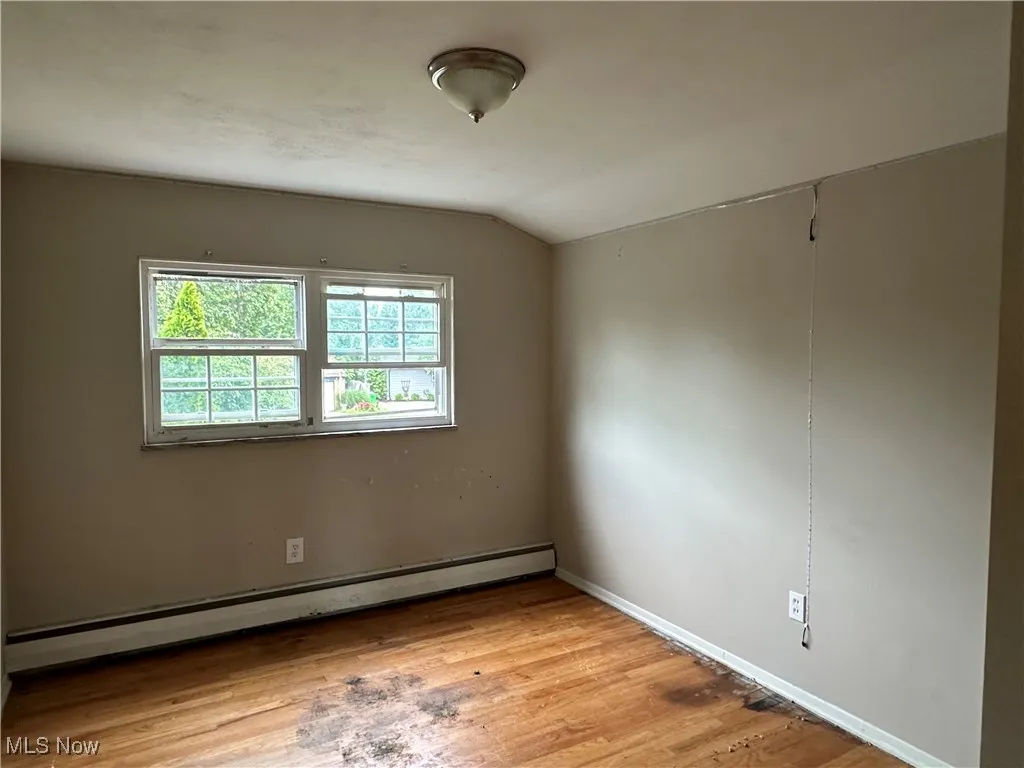 Spare room featuring a baseboard heating unit, vaulted ceiling, and light wood finished floors