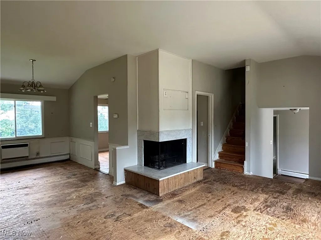 Unfurnished living room with vaulted ceiling, stairs, a decorative wall, a multi sided fireplace, and wainscoting
