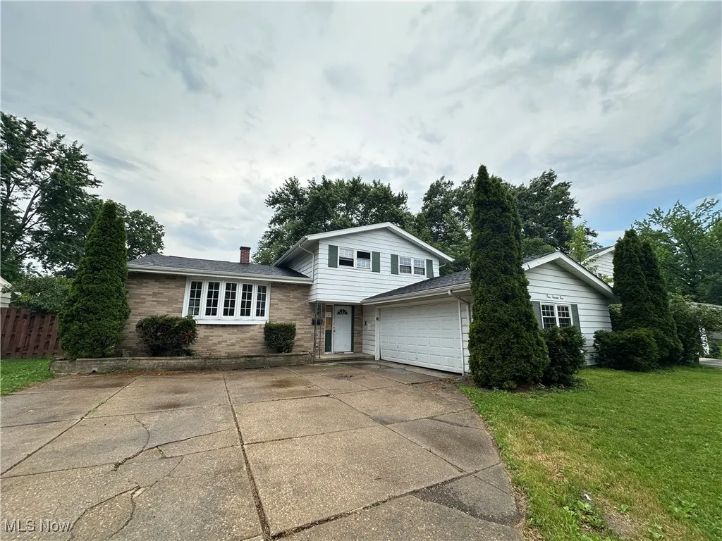 Tri-level home with driveway, brick siding, a chimney, an attached garage, and roof with shingles