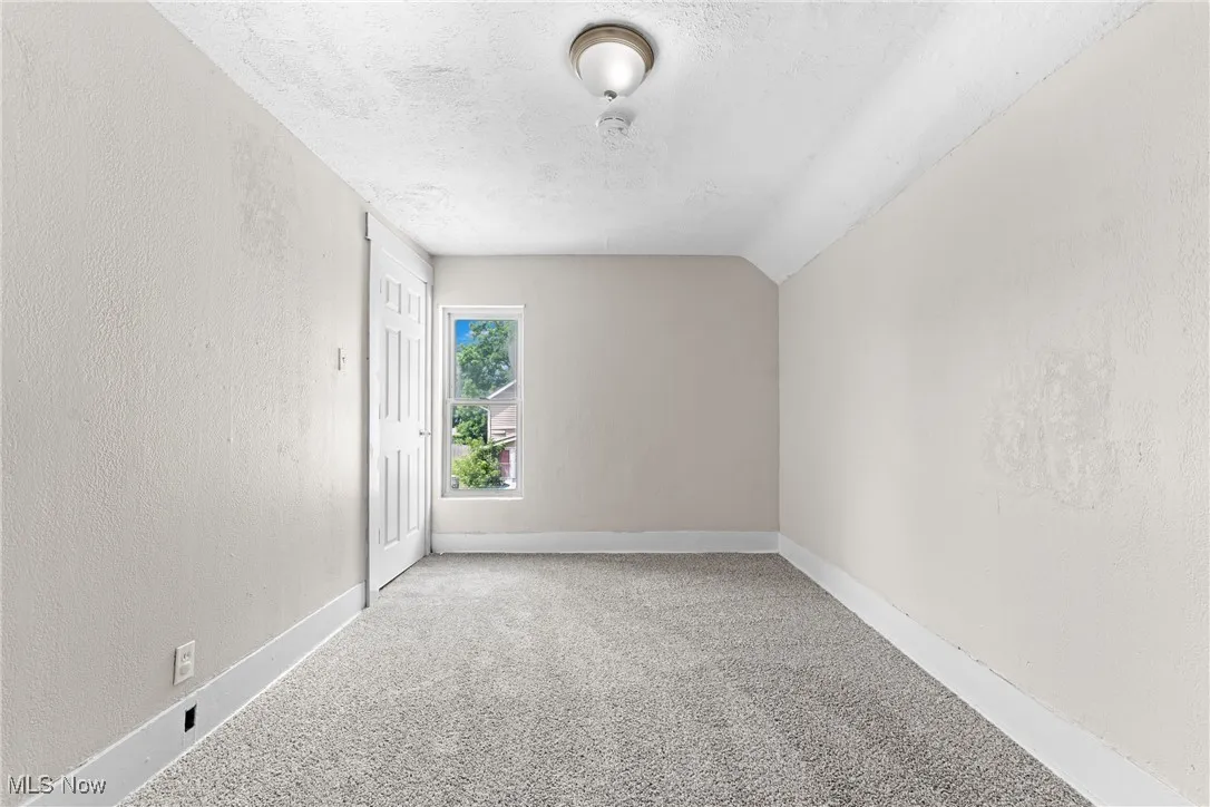 Carpeted empty room with a textured wall, a textured ceiling, and lofted ceiling