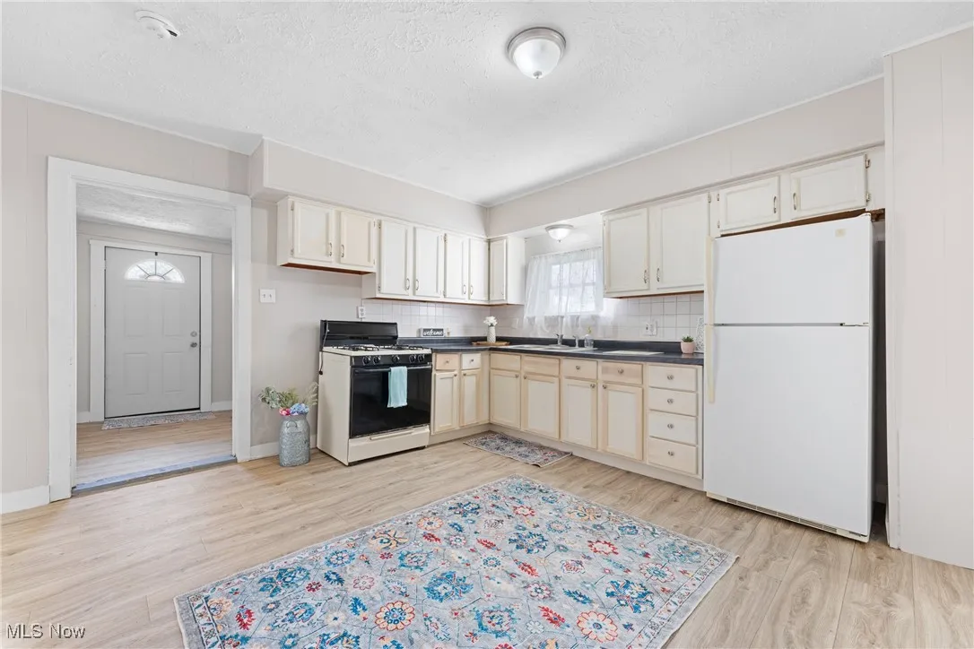 Kitchen featuring freestanding refrigerator, range with gas stovetop, a textured ceiling, dark countertops, and light wood finished floors