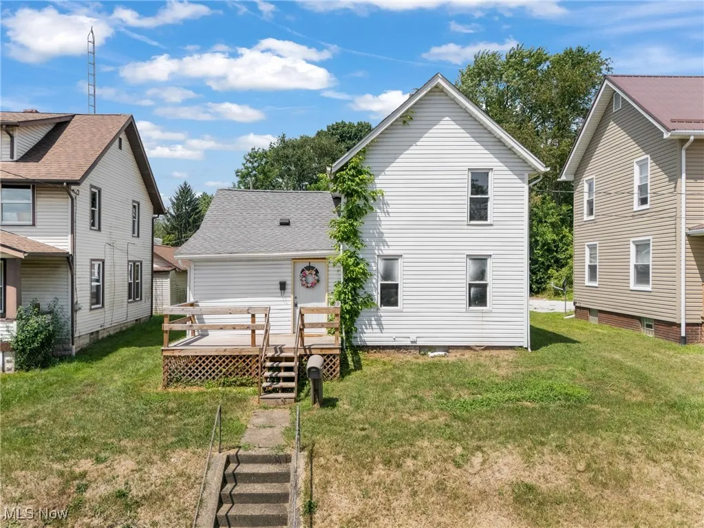 Rear view of house featuring a wooden deck, a yard, a shingled roof, and stairway