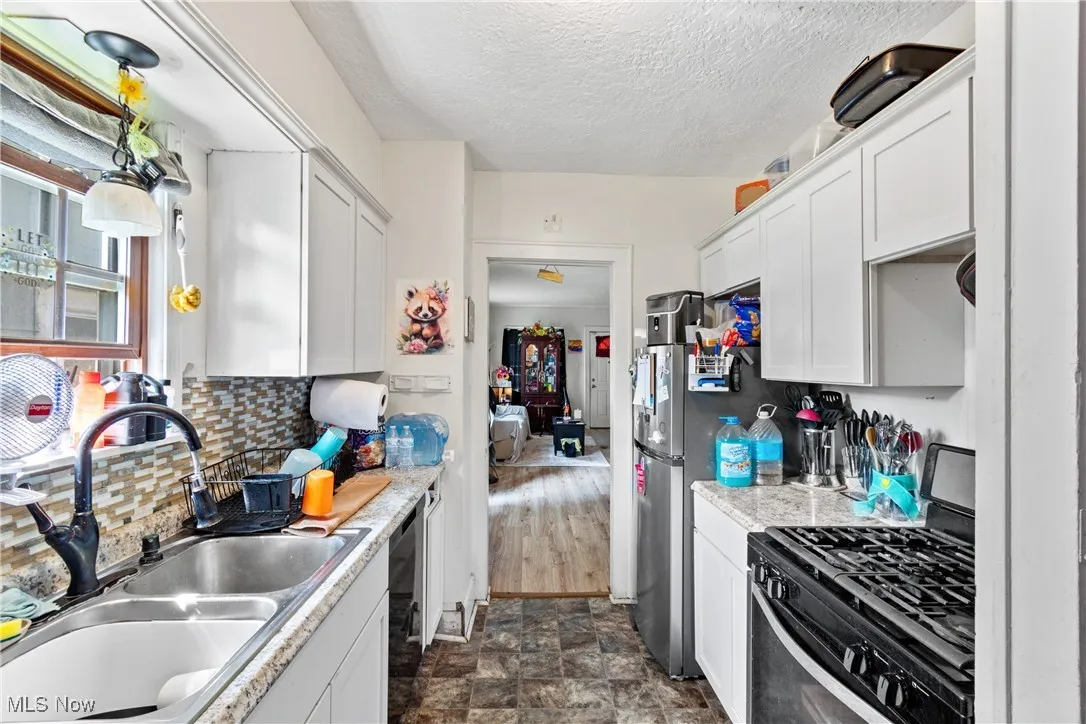 Kitchen with stainless steel range with gas cooktop, a textured ceiling, white cabinetry, light countertops, and stone finish floors