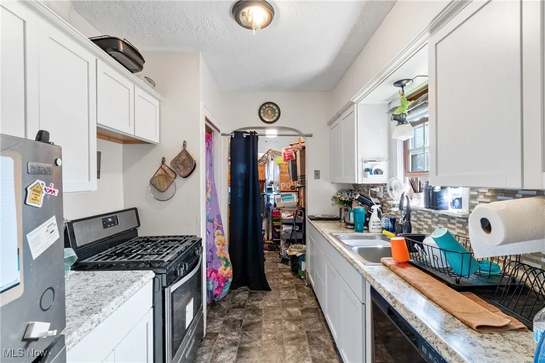 Kitchen featuring stainless steel range with gas stovetop, fridge, white cabinetry, a textured ceiling, and tasteful backsplash