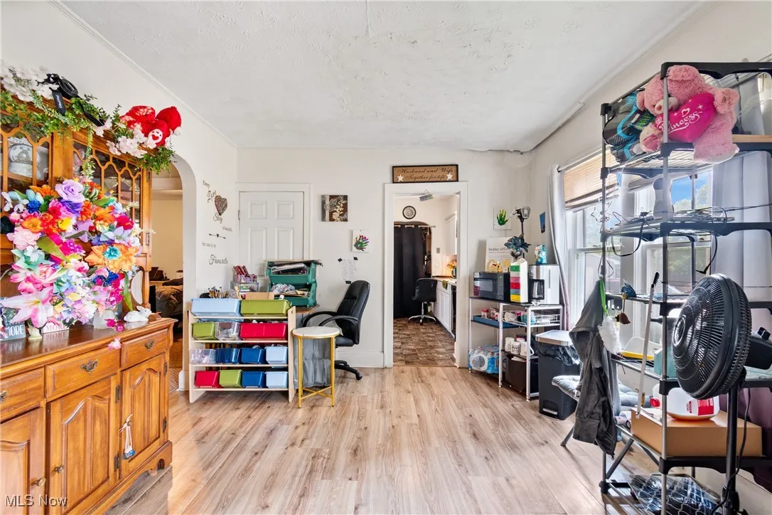Home office with light wood-type flooring, arched walkways, and a textured ceiling