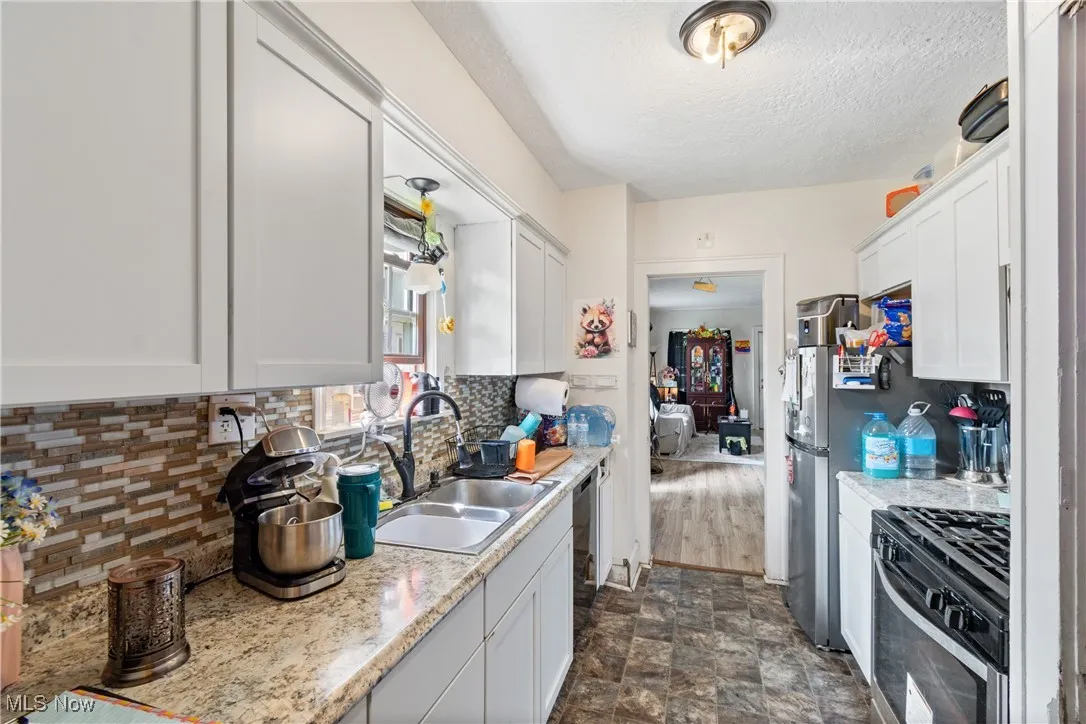 Kitchen featuring gas stove, tasteful backsplash, white cabinets, a textured ceiling, and stone finish floors