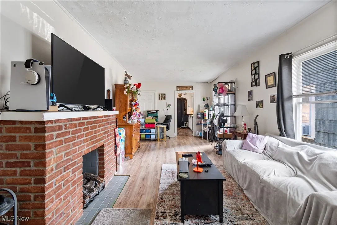 Living room with wood finished floors, a brick fireplace, and a textured ceiling