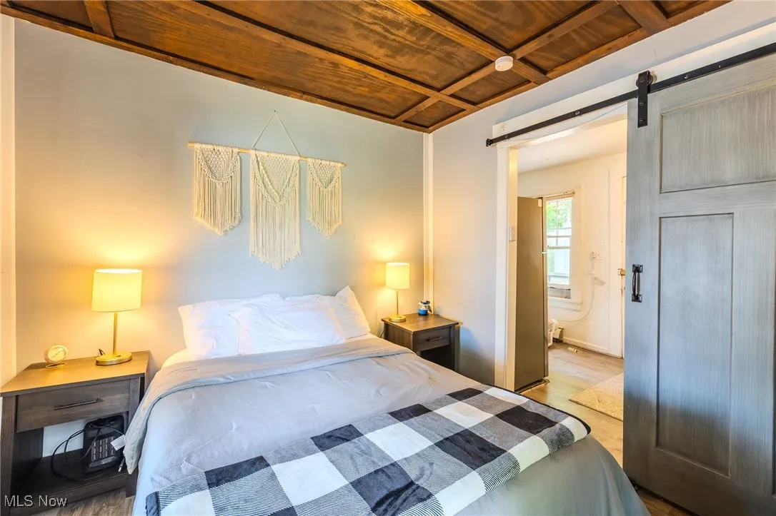 Bedroom with wood finished floors, a barn door, wood ceiling, and ensuite bathroom