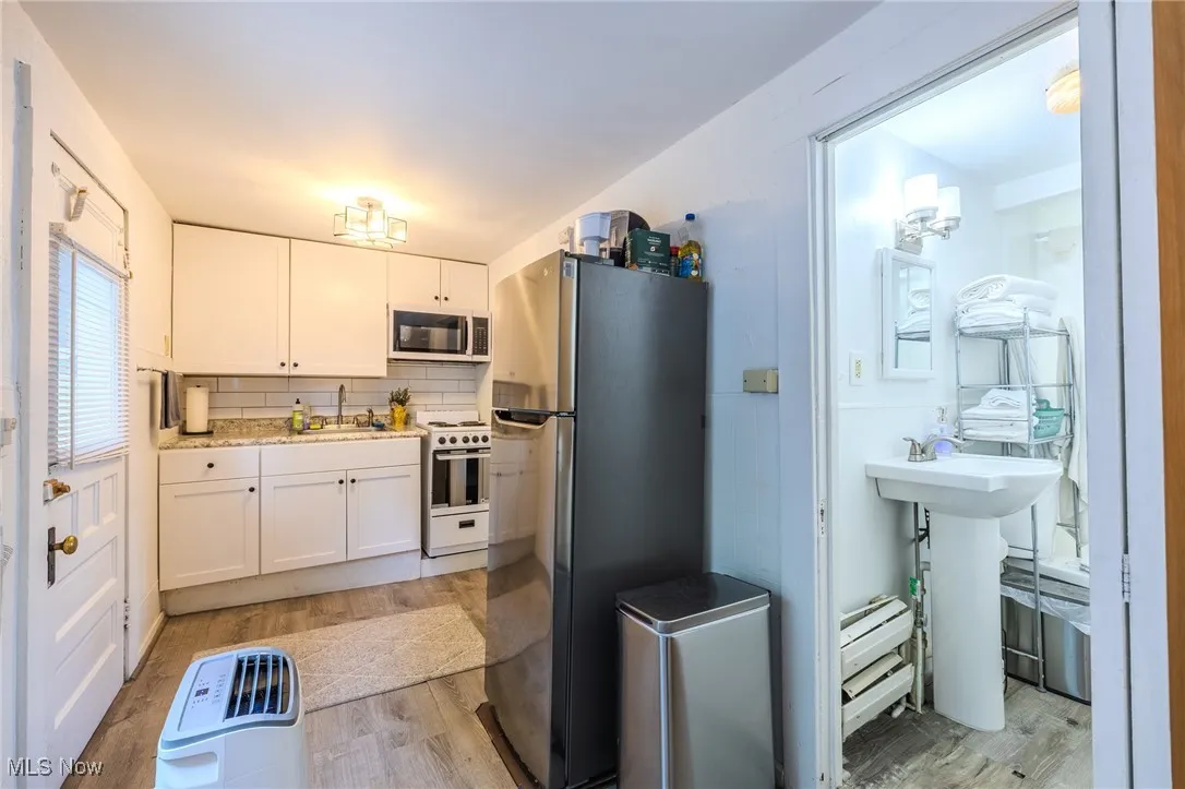 Kitchen featuring freestanding refrigerator, decorative backsplash, white cabinets, light wood finished floors, and white range oven