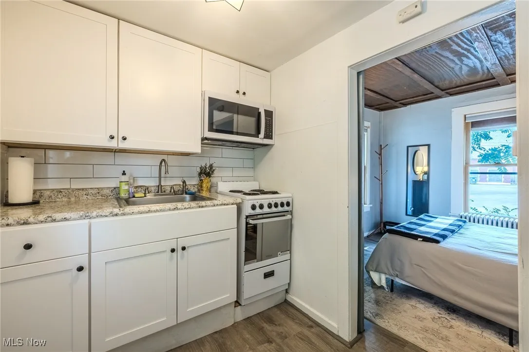 Kitchen with decorative backsplash, white appliances, dark wood-style floors, white cabinetry, and light stone counters