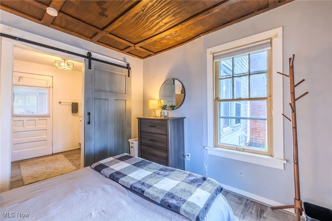 Bedroom featuring wood ceiling, a barn door, wood finished floors, and multiple windows