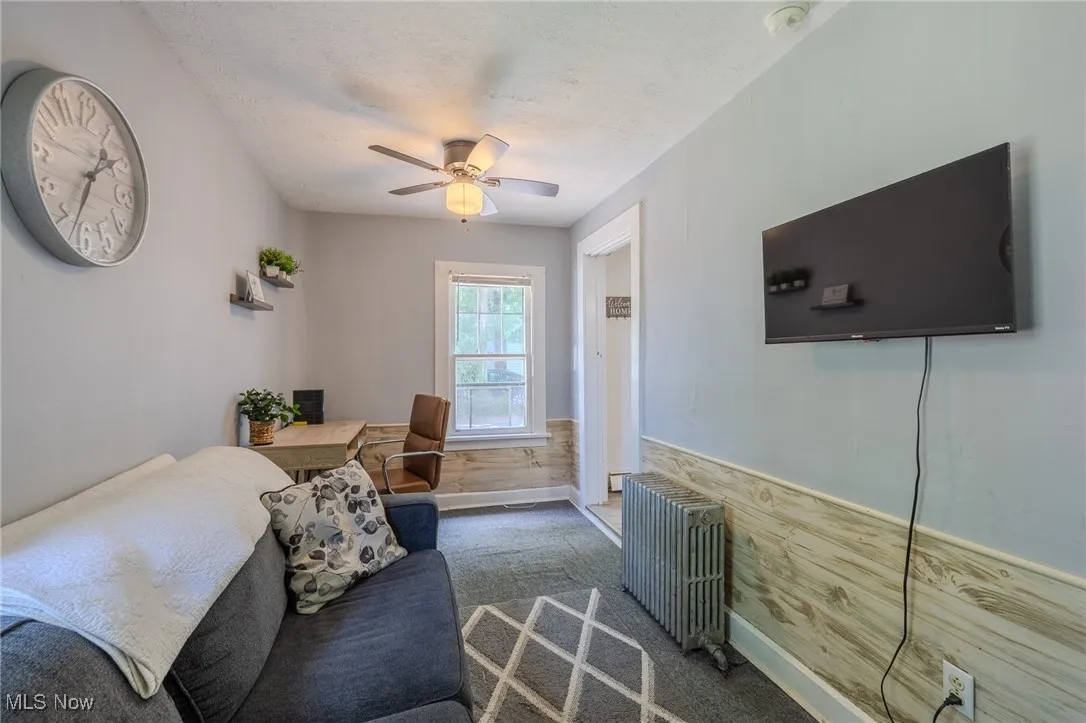 Carpeted living area featuring radiator, ceiling fan, a textured ceiling, and wainscoting