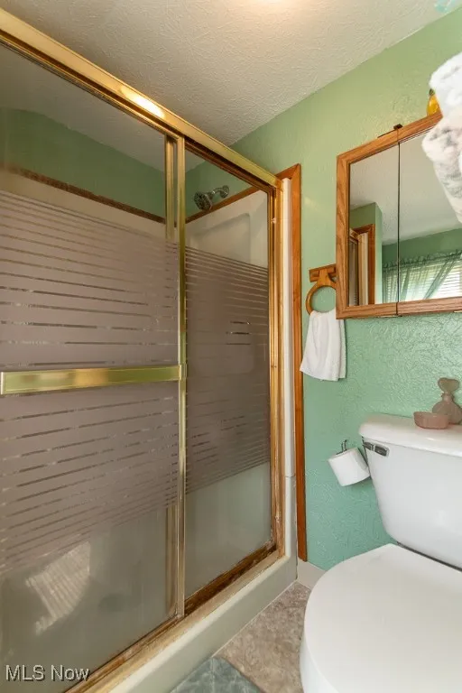 Bathroom featuring a textured wall, a shower stall, a textured ceiling, and tile patterned flooring