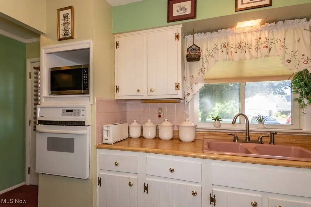 Kitchen featuring white oven, backsplash, stainless steel microwave, white cabinetry, and light countertops