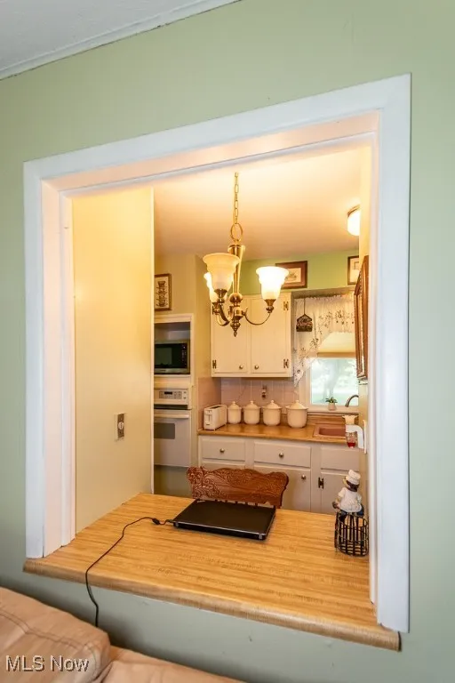Kitchen featuring a chandelier, white cabinetry, decorative backsplash, white oven, and decorative light fixtures