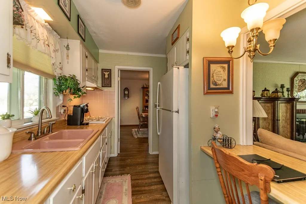 Kitchen featuring freestanding refrigerator, ornamental molding, light countertops, dark wood-style floors, and a chandelier
