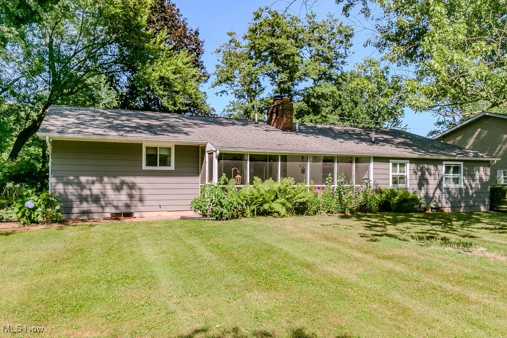 Back of property featuring a chimney, a lawn, and a sunroom