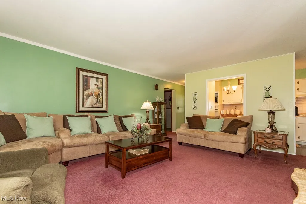 Carpeted living area featuring a chandelier and crown molding