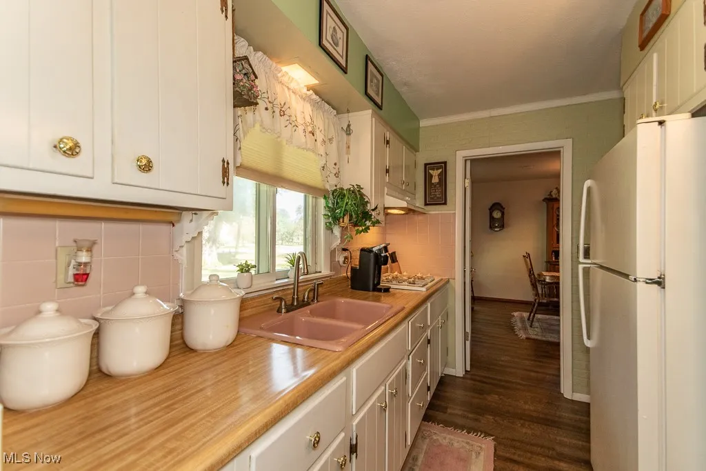 Kitchen featuring freestanding refrigerator, light countertops, white cabinets, dark wood finished floors, and ornamental molding