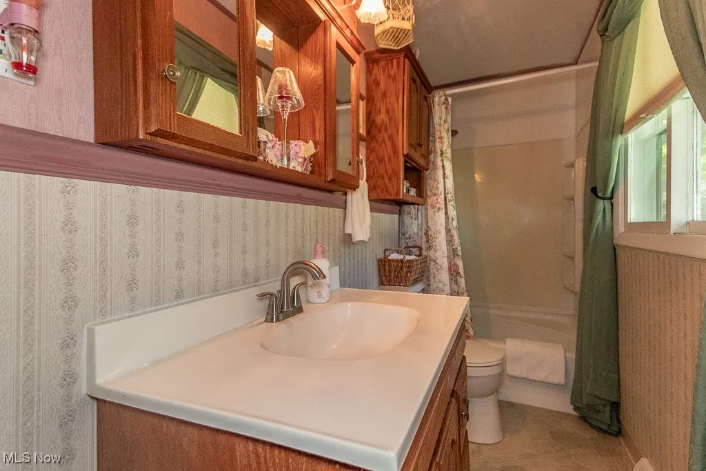 Full bath featuring wallpapered walls, vanity, and shower / tub combo with curtain