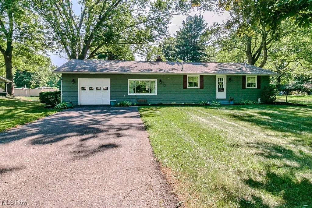Ranch-style house featuring asphalt driveway, an attached garage, entry steps, a front lawn, and a chimney