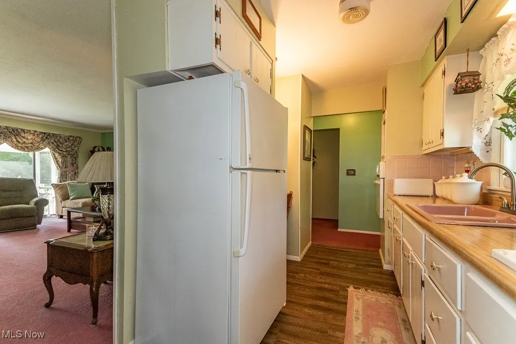 Kitchen featuring freestanding refrigerator, light countertops, backsplash, and white cabinetry