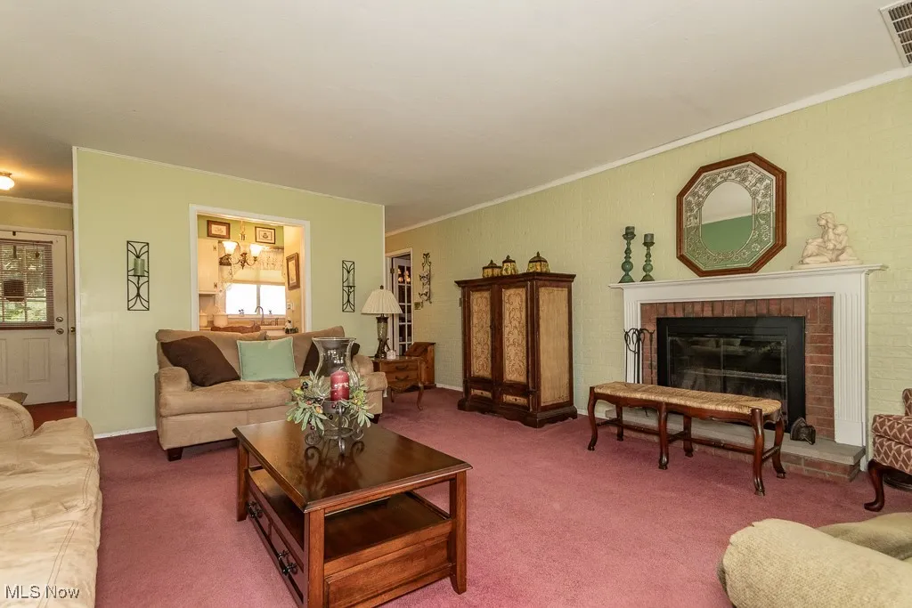 Living area with ornamental molding, carpet, a chandelier, and a fireplace