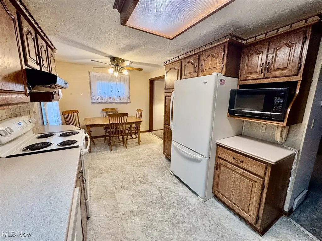 Kitchen featuring white appliances, a textured ceiling, tasteful backsplash, a ceiling fan, and light countertops